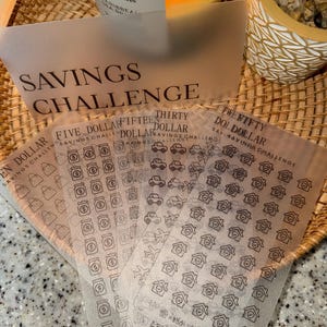 May include: A collection of translucent savings challenge cards with various dollar amounts and icons. The cards are labeled "Savings Challenge" and feature illustrations of purses, jars, cars, and houses. The total savings amount is $2250.