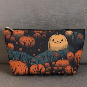 Könnte beinhalten: Eine schwarze Reißverschlusstasche mit einem Halloween-Motiv aus orangefarbenen Kürbissen mit lächelnden Gesichtern auf dunkelgrünem Hintergrund.