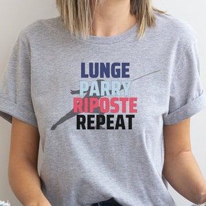 May include: A gray t-shirt with the text "LUNGE PARRY RIPOSTE REPEAT" in blue, pink, and black. A silhouette of a person fencing is shown above the text.
