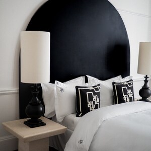 May include: A white bed with a black headboard shaped like a half circle. The headboard has a white and black geometric pattern. There are two white lamps on bedside tables next to the bed.