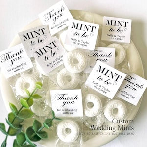 May include: A collection of individually wrapped white ring-shaped mints, each accompanied by a square paper tag. The tags feature black text reading MINT to be, Thank you for celebrating with us, and the names Sally & Taylor with date 10.17.2026.