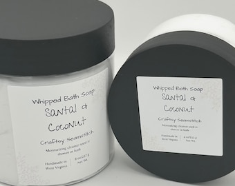 May include: Two jars of whipped bath soap with black lids. The labels read "Santal & Coconut" and "Craftsy Seamstitch." The jars contain a white, fluffy soap. One jar is upright, and the other is on its side.
