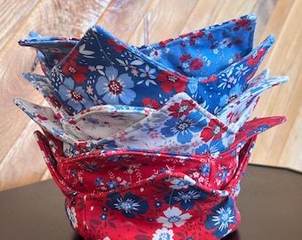 May include: A stack of three fabric bowl cosies featuring floral patterns in red, white, and blue. The top cosy is blue with red and white flowers, the middle is white with blue and red flowers, and the bottom cosy is red with blue and white flowers.