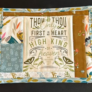 Può includere: Un oggetto di tessuto rettangolare con un design patchwork. Il pannello centrale presenta il testo "THOU & THOU Only FIRST IN MY HEART HIGH KING OF heaven". I pannelli circostanti hanno motivi floreali e geometrici nei toni del blu, verde e marrone.