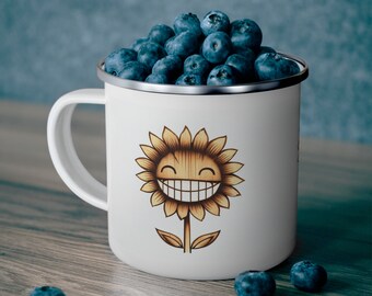 Könnte beinhalten: Weiße Emaille-Campingtasse mit einem lächelnden Sonnenblumen-Design. Die Tasse ist mit Blaubeeren gefüllt.