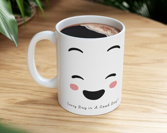 Könnte beinhalten: Weiße Keramik-Kaffeetasse mit einem lächelnden Comic-Gesicht und dem Text "Every Day is A Good Day!!" auf dem Boden. Die Tasse ist mit Kaffee gefüllt.