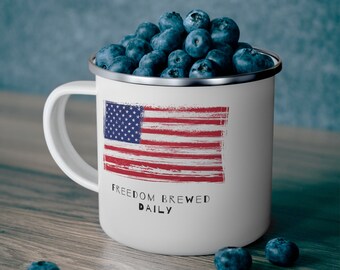 Könnte beinhalten: Eine weiße Emailletasse mit einem rot-weiß-blauen amerikanischen Flaggenmuster und dem Text "Freedom Brewed Daily". Die Tasse ist mit Blaubeeren gefüllt.