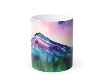 Könnte beinhalten: Eine weiße Keramiktasse mit einem farbenfrohen Aquarelldesign eines Gebirges mit einem rosa, violetten und blauen Himmel. Das Gebirge ist von grünen Bäumen umgeben.