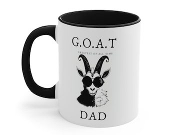Könnte beinhalten: Weiße Keramik-Kaffeetasse mit schwarzem Henkel und schwarzem Rand. Die Tasse zeigt eine Schwarzweißillustration einer Ziege mit Sonnenbrille und dem Text "G.O.A.T. Greatest of All Time Dad".