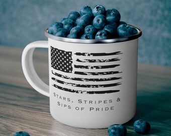 Könnte beinhalten: Eine weiße Emailletasse mit einem schwarz-weißen, abgenutzten Design der amerikanischen Flagge. Der Text "Stars, Stripes & Sips of Pride" ist unter der Flagge aufgedruckt. Die Tasse ist mit Blaubeeren gefüllt.