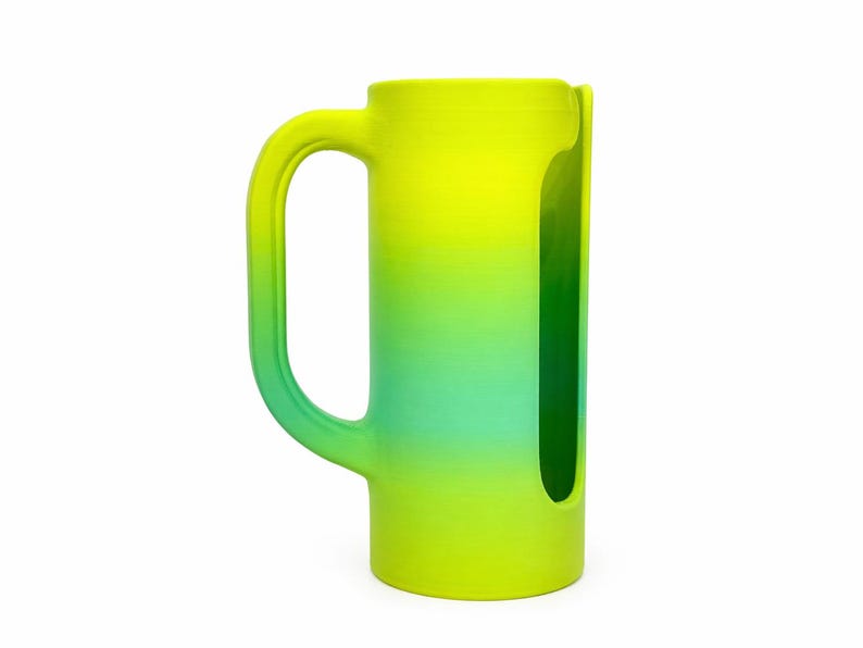 May include: A tall, cylindrical mug with a large handle, featuring a gradient of yellow to teal. The mug has a unique cutout on one side. The design is modern and the color scheme is vibrant.