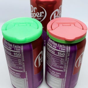 May include: Three aluminum soda cans topped with circular plastic lids in neon green, light pink, and iridescent purple. The cans feature red and purple labels with white text including Dr Pepper branding and nutrition facts panels.