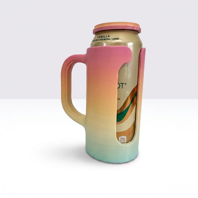May include: A gradient-colored can cooler with a handle, transitioning from pink to yellow to teal. The cooler holds a can with the word "DT" visible. The can is labeled "Vanilla with other natural flavors".