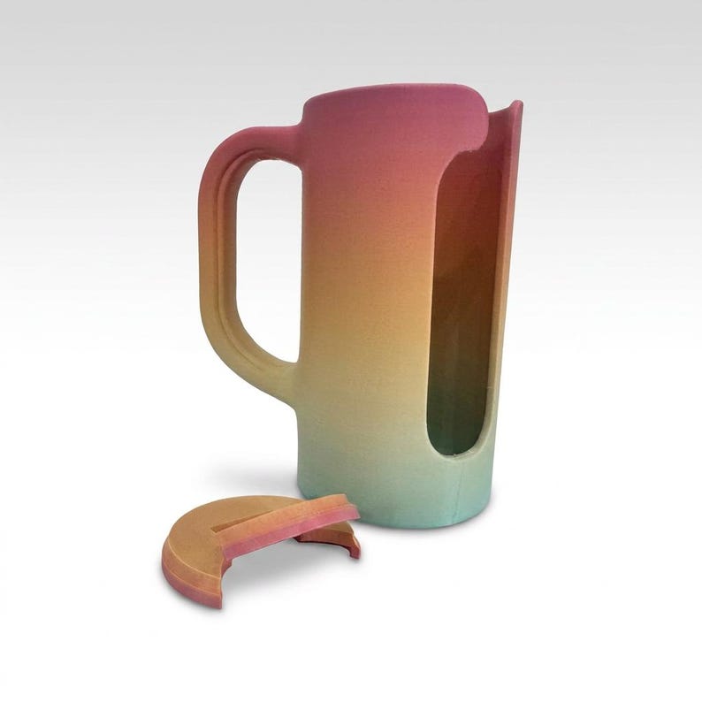 May include: A tall, cylindrical pitcher with a handle and a partial cutout, featuring a gradient of colors from pink to yellow to blue. A matching lid rests nearby. The pitcher is likely ceramic or a similar material.