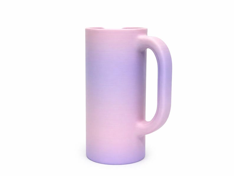 May include: A tall, cylindrical mug with a large handle. The mug features a gradient color scheme, transitioning from pink at the base to lavender at the top. The mug is made of a solid material and has a smooth finish.