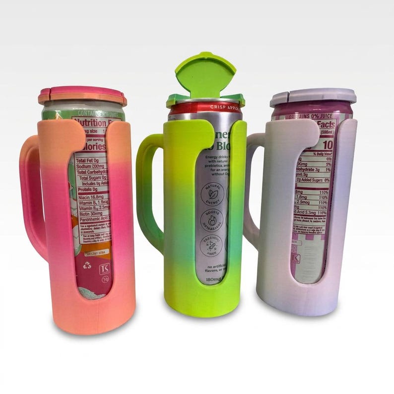 May include: Three colorful can holders with handles, each holding a beverage can. The holders are in shades of pink, green, and white, with a cutout to view the can's label. One holder has a green lid.