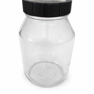 May include: A clear glass jar with a black lid. The jar has a wide body and a rounded base. The black lid is made of a ribbed material. The jar is empty and sits on a white background.