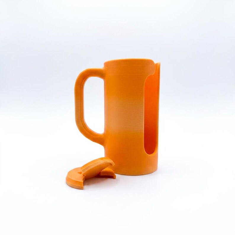 May include: An orange mug with a handle and a large cutout on the side. A detached orange lid sits in front of the mug. The mug is made of a solid material and has a cylindrical shape.