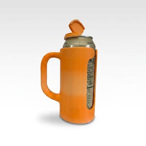 May include: Orange plastic can holder with a handle, designed to hold a standard beverage can. The holder has an attached lid that can be opened and closed. The can's label is visible through a cutout on the side. The holder is designed to keep the beverage cold.