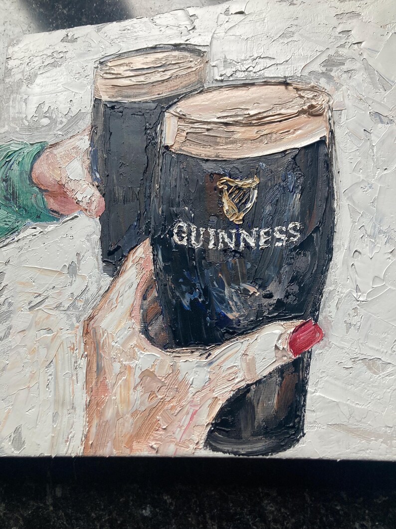May include: An oil painting with thick impasto texture depicting two dark glasses of stout beer. The glasses feature the gold harp logo and the white text GUINNESS. One glass is held by a hand with red nail polish, and the other by a sleeve.