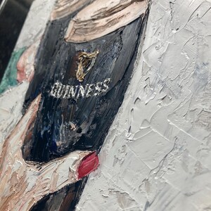 May include: An oil painting on canvas featuring a thick, textured impasto application of paint. The artwork depicts a dark glass of Guinness stout with its signature cream-colored head, accented by a gold harp logo and the white text GUINNESS.