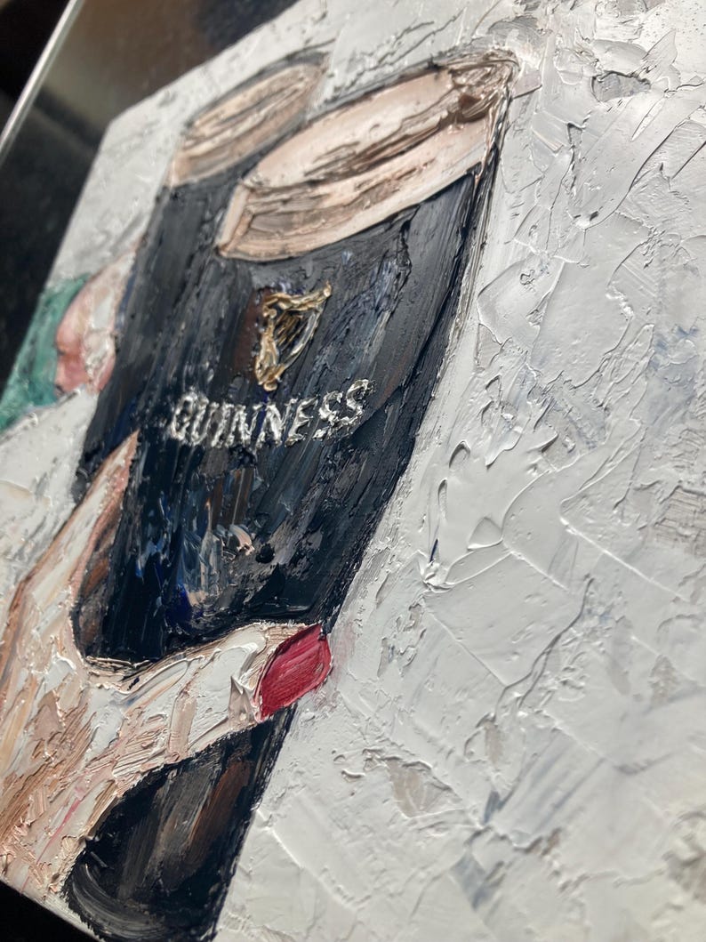 May include: An oil painting on canvas featuring a thick, textured impasto application of paint. The artwork depicts a dark glass of Guinness stout with its signature cream-colored head, accented by a gold harp logo and the white text GUINNESS.