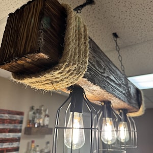 May include: A rustic wooden beam light fixture with a rope accent and four caged light bulbs. The fixture is hanging from the ceiling and has a farmhouse style.
