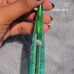 May include: A green crochet hook with a clear resin handle, featuring embedded white star and animal-shaped embellishments. The hook is 4.0mm. The handle has a glittery, iridescent effect. The Instagram handle @CIRNIA_CRAFTS is visible.