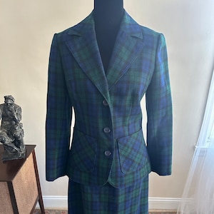 Könnte beinhalten: Ein grüner und blauer karierter Rockanzug mit einer taillierten Jacke und einem knielangen Rock.