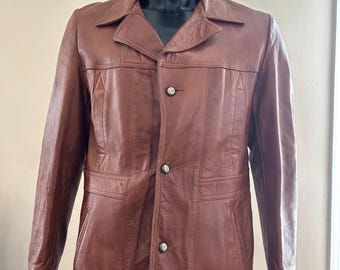 May include: A brown leather jacket with a button-up front and a collar. The jacket has two pockets on the front and a single button on each cuff.