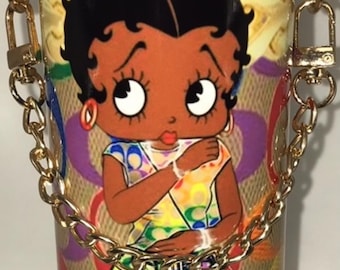 May include: A colourful tumbler with a gold chain handle. The tumbler features a cartoon image of a Black woman with a Coach New York logo in the background.