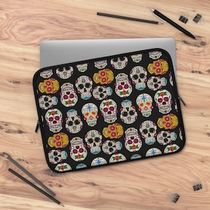May include: A black laptop sleeve with a colorful sugar skull pattern. The skulls are decorated with flowers and other details.