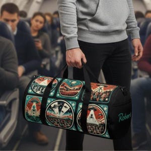 May include: Black duffel bag with a colorful, retro-style alien-themed design. The bag features multiple circular illustrations of UFOs and extraterrestrials. The name "Robert" is printed in teal on the side of the bag.