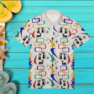 Könnte beinhalten: Weißes Poloshirt mit Retro-Muster, das schwarze Katzen, geometrische Formen und farbige Sternausbrüche zeigt. Das Muster umfasst Rechtecke und Sternausbrüche in Rot, Blau, Gelb und Grün. Das Shirt hat einen Kragen und kurze Ärmel.