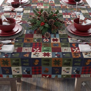 May include: A rectangular tablecloth featuring a patchwork grid pattern with various seasonal motifs including pine trees, mountains, acorns, plaid squares, and star shapes in shades of red, green, blue, and brown, set with red bowls and white napkins.
