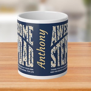 以下が含まれることがあります： 青い背景に金色の文字が書かれた白いセラミック製のコーヒーカップ。テキストは「Awesome Stepdad Anthony」と「Some Dad」で、小さな金色の星のパターンが描かれています。