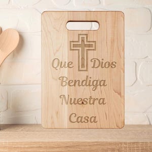 May include: A wooden cutting board with a cross and the text "Que Dios Bendiga Nuestra Casa" engraved on it.