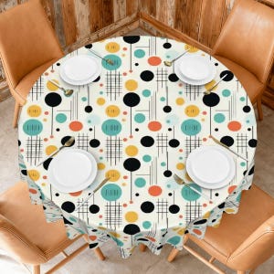 May include: A round tablecloth with a cream background featuring a mid-century modern pattern of black, teal, and yellow circles, thin black vertical lines, and small orange dots. Four white plates and four sets of silverware are arranged on top.