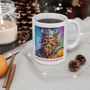 May include: White ceramic coffee mug with a colorful illustration of a Viking warrior with a beard and helmet. The text "VIKING BLOOD IS IN MY DNA" is printed on the bottom of the mug.