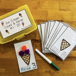 May include: A set of ice cream cone counting cards with pom-poms for counting. The cards have a picture of an ice cream cone and the number written out and in numerals. The cards are in a yellow plastic container with the words "Ice Cream Count & Write #1 - 20".