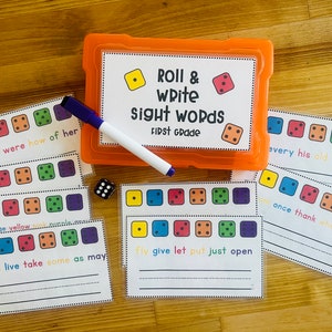 May include: A set of colorful dice and cards for a first grade sight word game. The game includes a plastic storage container with the words "Roll & Write Sight Words First Grade" printed on the lid. The cards have different colored dice with sight words written on them.