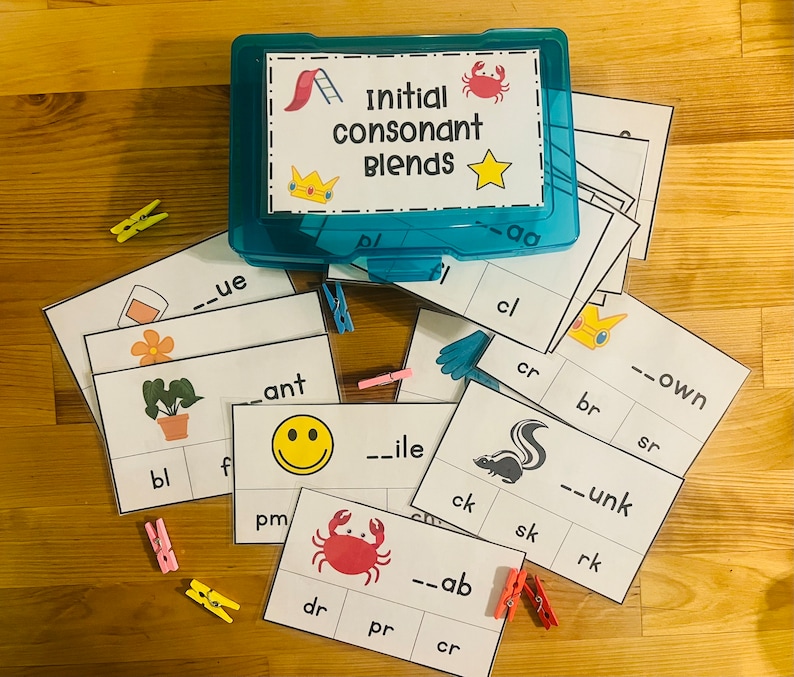 May include: A set of educational flashcards for learning initial consonant blends. The cards feature colorful illustrations and the words "Initial consonant blends" in a blue box. The cards are arranged on a wooden surface with clothespins.