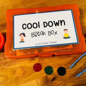 May include: An orange plastic box labeled "Cool Down Break Box" with illustrations of children. Includes a red container, blue tongs, and colorful discs on a wooden surface. The box is from "Little Minds Learning".