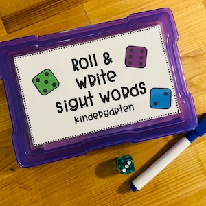 May include: A purple plastic storage box with a white card that says "Roll & Write Sight Words Kindergarten". There are three dice with different colored dots on them. One die is green, one is purple, and one is blue.