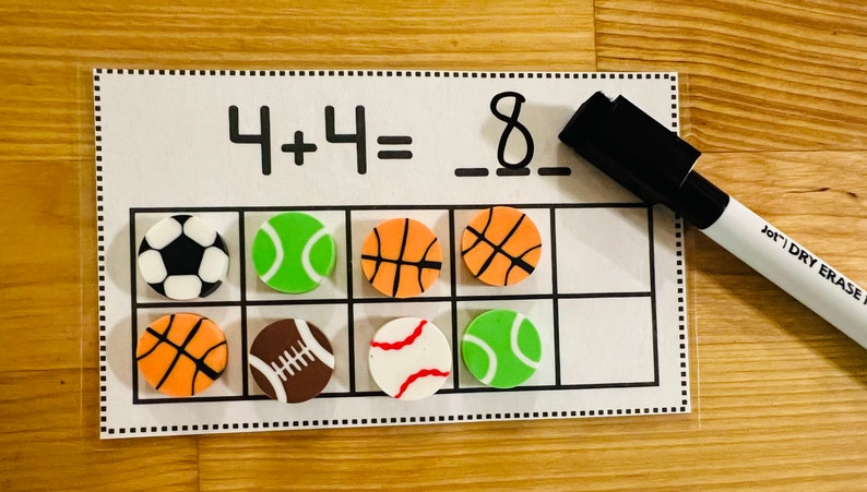 May include: A white dry-erase board with a math problem written on it: 4 + 4 = 8. There are eight colorful sports-themed erasers on the board, including soccer balls, basketballs, baseballs, and tennis balls.