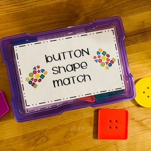 May include: A purple plastic container with a white label that says "button shape match". There are colorful buttons inside the container. There are three buttons outside the container: a purple pentagon, a yellow circle, and a red square.