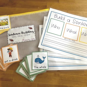 Puede incluir: Materiales educativos para la construcción de oraciones. Incluye tarjetas didácticas con ilustraciones y texto, una hoja de trabajo con indicaciones de "Quién, Qué, Dónde" y una bolsa de malla. Las tarjetas didácticas presentan imágenes como un niño bebiendo y una ballena.