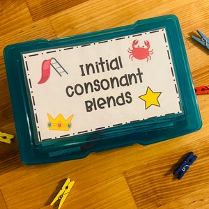 May include: A blue plastic storage box with a white label that says "Initial Consonant Blends". The label has a red crab, a yellow star, a red and yellow slide, and a gold crown with a red jewel.