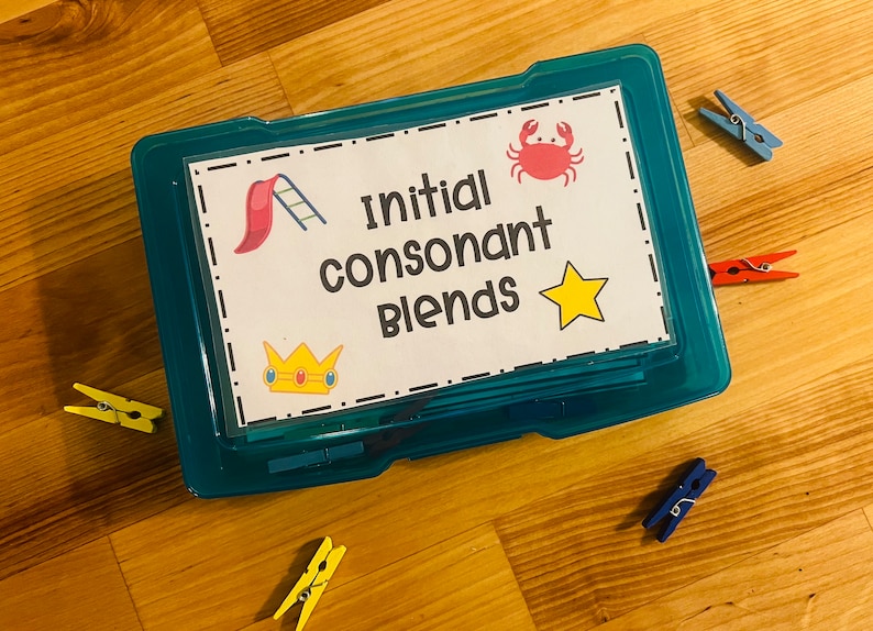 May include: A blue plastic storage box with a white label that says "Initial Consonant Blends". The label has a red crab, a yellow star, a red and yellow slide, and a gold crown with a red jewel.