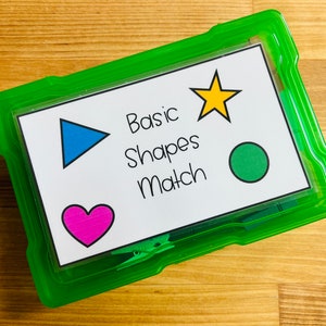 May include: A green plastic storage container with a white label that says "Basic Shapes Match". The label has a blue triangle, a yellow star, and a green circle.